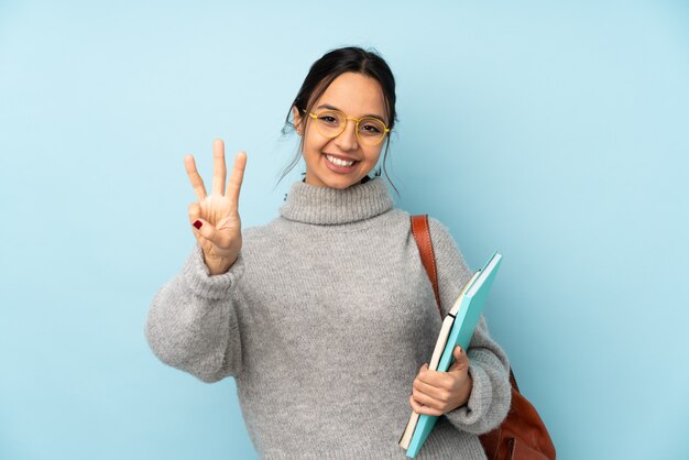 Jonge gemengde rasvrouw die naar school gaan die op blauwe gelukkige muur wordt geïsoleerd en drie met vingers telt