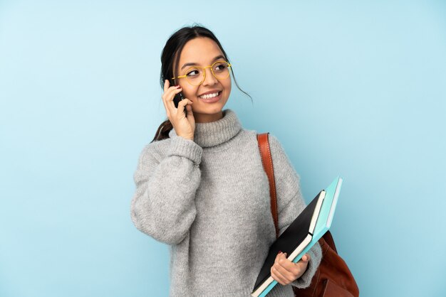 Jonge gemengde rasvrouw die naar school op blauwe muur gaan die een gesprek met de mobiele telefoon met iemand houden