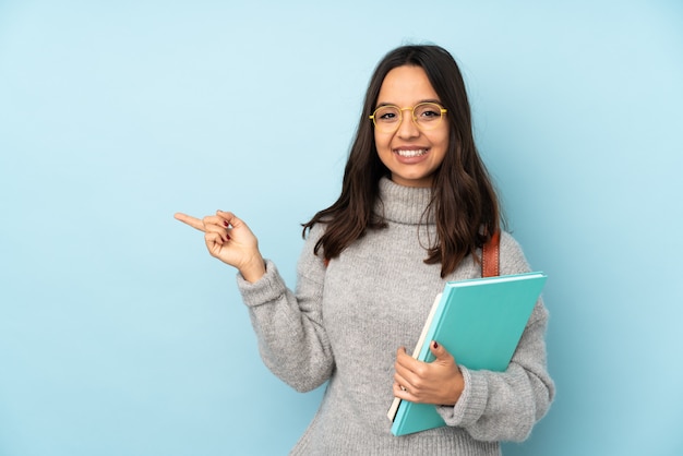 Jonge gemengde rasvrouw die naar school op blauwe muur gaan die vinger aan de kant richten