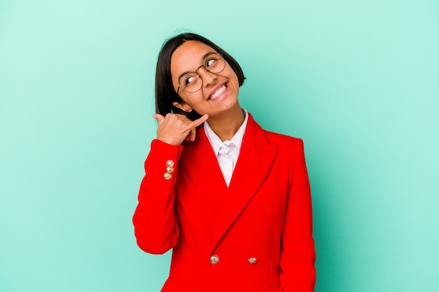 Jonge gemengde rasvrouw die op blauwe achtergrond wordt geïsoleerd die een mobiel telefoongesprekgebaar met vingers toont.