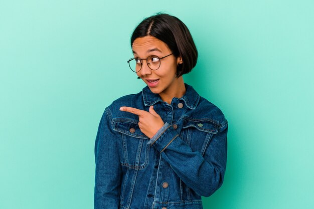 Jonge gemengde rasvrouw die op blauwe achtergrond wordt geïsoleerd kijkt opzij glimlachend, vrolijk en aangenaam.