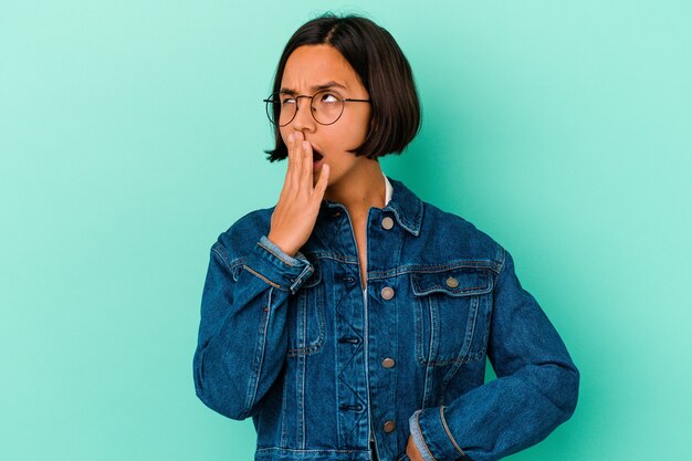 Jonge gemengde rasvrouw die op blauwe muur wordt geïsoleerd die geeuwt die een moe gebaar toont dat mond behandelt met hand.