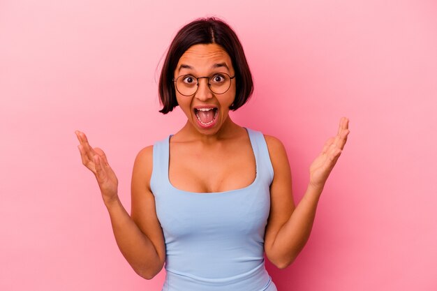 Jonge gemengde rasvrouw die op roze muur wordt geïsoleerd die een aangename verrassing ontvangt, opgewonden en handen opheft.