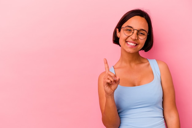 Jonge gemengde rasvrouw die op roze muur wordt geïsoleerd die nummer één met vinger toont.