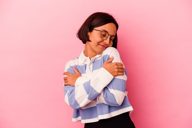 Jonge gemengde rasvrouw die op roze omhelzingen wordt geïsoleerd als achtergrond, onbezorgd en gelukkig glimlachen.