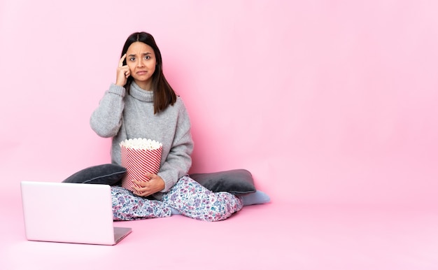 Jonge gemengde rasvrouw die popcorn eet tijdens het kijken naar een film op de laptop die een idee denkt
