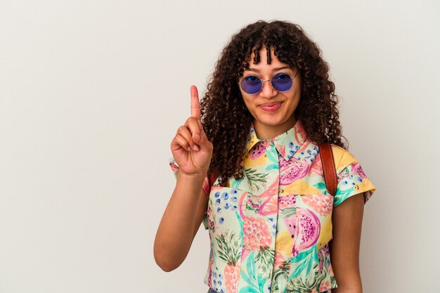 Jonge gemengde rasvrouw die zonnebril draagt die een geïsoleerde vakantie neemt die nummer één met vinger toont.