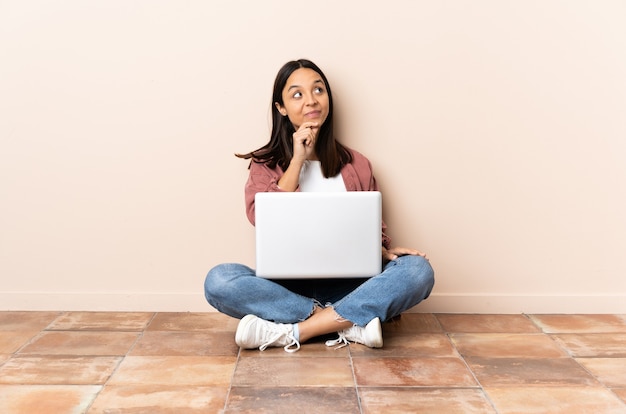 Jonge gemengde rasvrouw met laptopzitting op de vloer die een idee denken terwijl het opzoeken