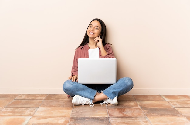 Jonge gemengde rasvrouw met laptopzitting op de vloer het lachen