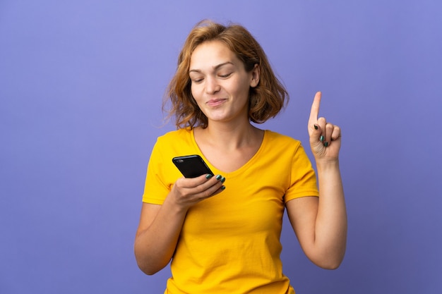 Jonge Georgische vrouw geïsoleerd op paarse achtergrond met behulp van mobiele telefoon en vinger opheffen