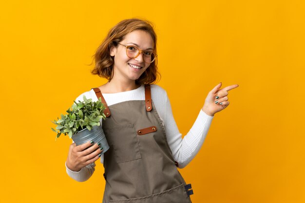 Jonge Georgische vrouw met een plant geïsoleerd op gele muur wijzende vinger naar de zijkant