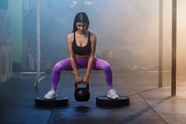 Jonge geschikte vrouw die oefening met domoren in de gymnastiek doet.