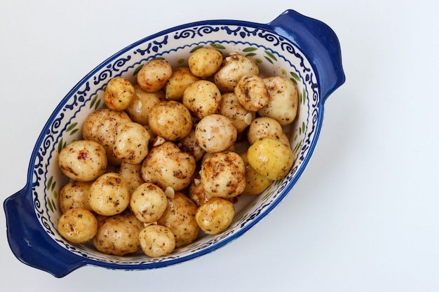 Jonge geschilde aardappelen in specerijen bereid voor roosteren in een keramische vorm op een witte ondergrond