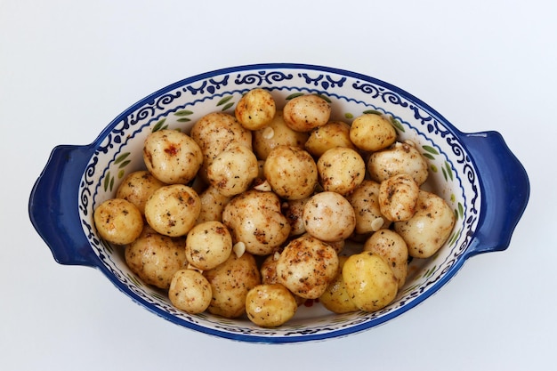 Jonge geschilde aardappelen in specerijen voorbereid op roosteren in een keramische vorm op een witte achtergrond