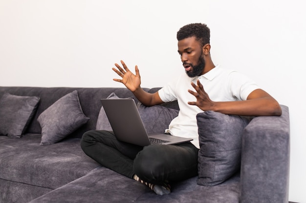 Jonge geschokt zwarte man online chatten op laptop met vriend thuis.