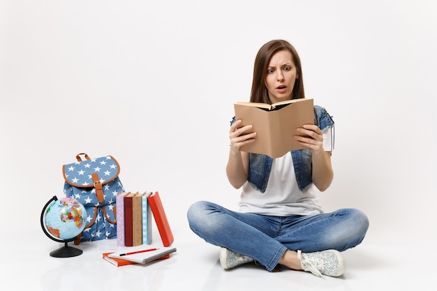 Jonge, geschokte, bange studente in spijkerkleding met boeklezing in de buurt van globe, rugzak, schoolboeken