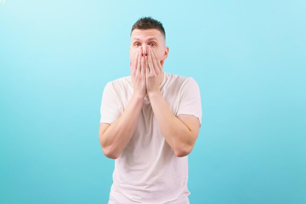 Jonge geschokte blanke man in een wit overhemd met zijn hand op zijn wang en mond op blauw