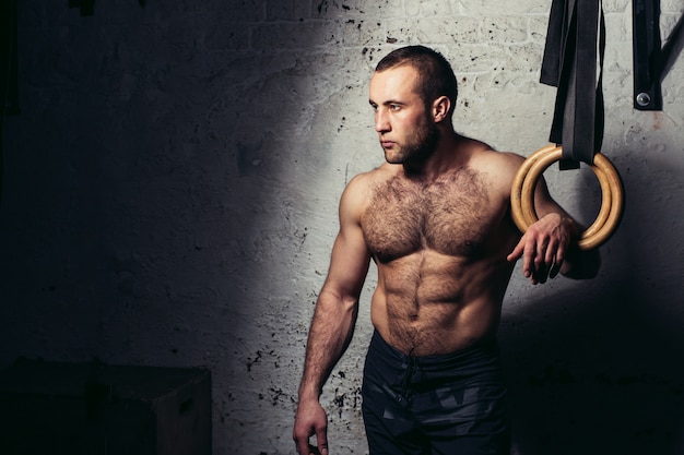 Jonge gespierde aantrekkelijke man naakte torso poseren tegen gymnastiek ringen