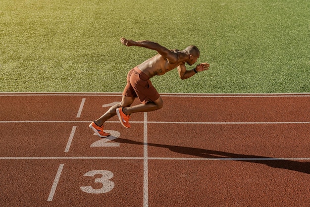 Foto jonge gespierde atleet begint te rennen op de stadionbaan