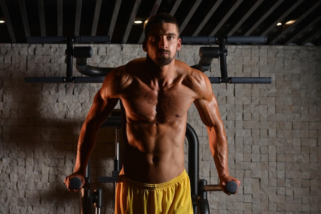 Jonge gespierde fitness bodybuilder doet zware oefening voor triceps en borst op parallelle staven in de sportschool