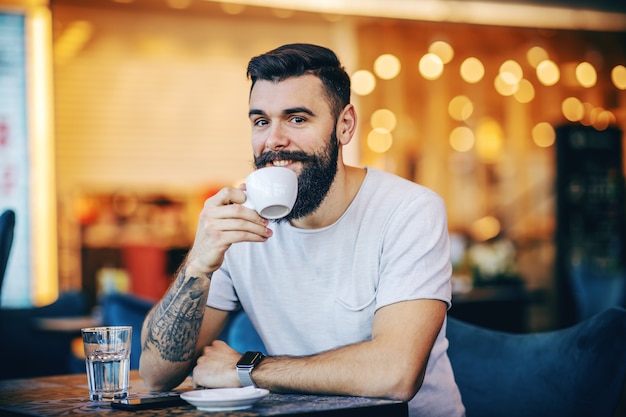 Jonge gespierde Kaukasische hipster koffie drinken in café. Hij heeft lunchpauze.