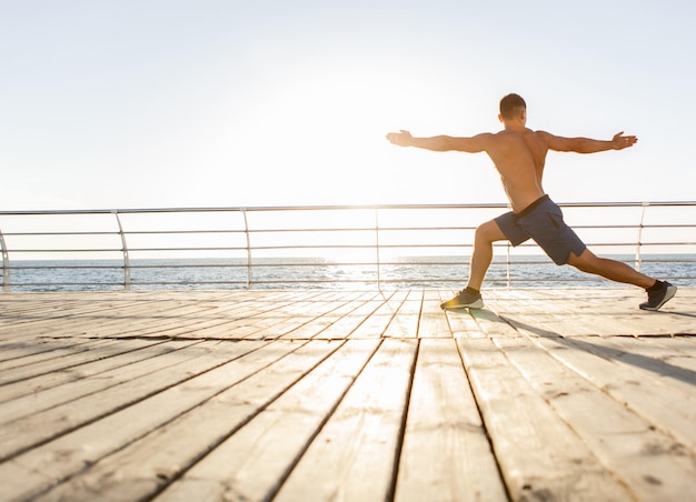 Jonge gespierde man die yoga asana beoefent bij zonsopgang op het strand