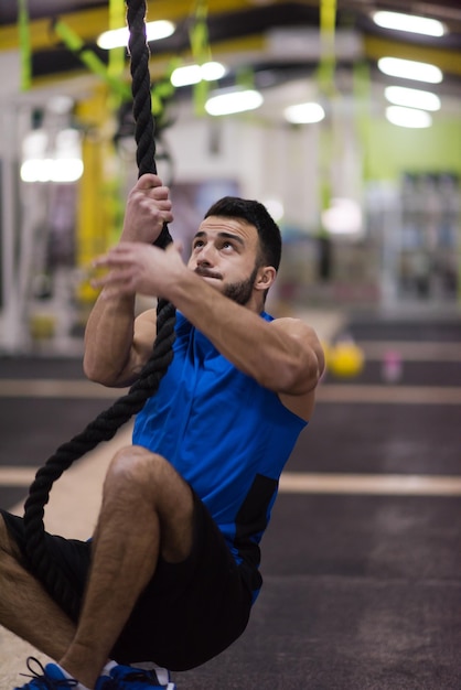 jonge gespierde man doet touw klimmen in cross fitness gym