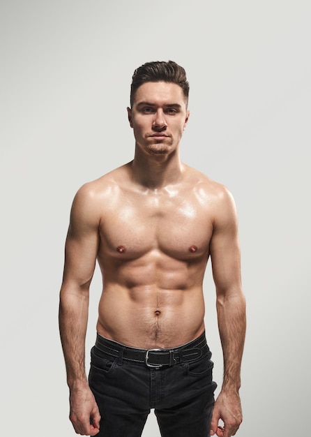 Jonge gespierde man staat zelfverzekerd zonder shirt.