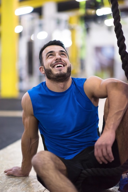 jonge gespierde man zitten en ontspannen voor touw klimmen in cross fitness gym