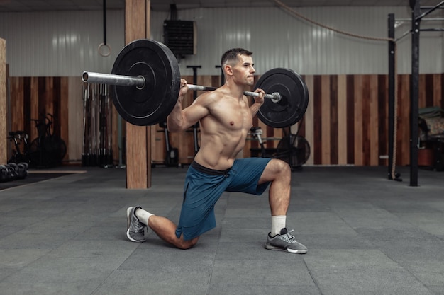 Jonge gespierde mannelijke bodybuilder doet lunges met een halter op zijn schouders in een moderne gezondheidsclub. bodybuilding en fitness