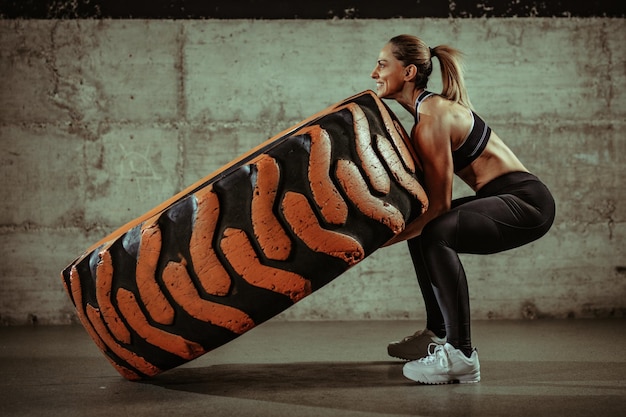 Jonge gespierde vrouw die een wielband omdraait tijdens een training in de sportschool.