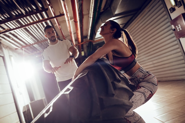 Foto jonge gespierde vrouw flipt een band op cross fit training met personal trainer in de garage.