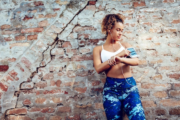 Jonge gespierde vrouw met koptelefoon opstaan tegen de muur en rusten na het joggen.