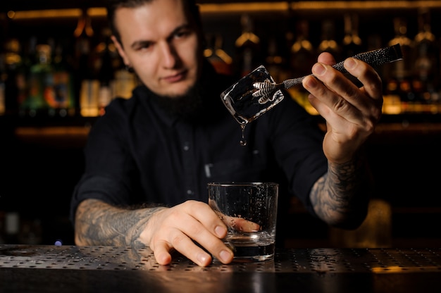 Jonge getatoeëerde barman zetten een ijsblokje in een cocktailglas