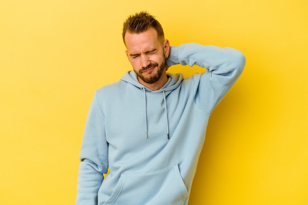 Jonge getatoeëerde blanke man geïsoleerd op gele muur met nekpijn als gevolg van stress, masseren en aanraken met de hand.