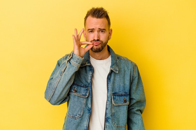 Foto jonge getatoeëerde blanke man geïsoleerd op gele muur met vingers op lippen die een geheim houden.