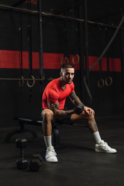 Jonge getatoeëerde man die sport doet in een sportschool met een rood shirt