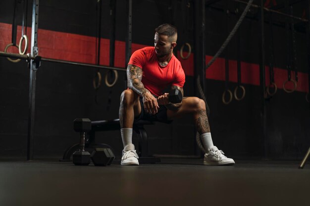 jonge getatoeëerde man die sport doet in een sportschool met een rood shirt