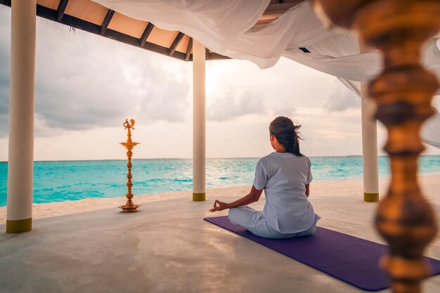 Jonge gezonde vrouw die yoga beoefent op het strand bij zonsondergang. Rust en concentratie, zen