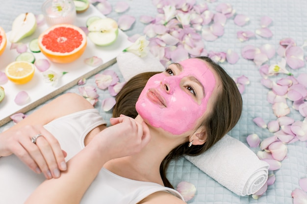 Jonge gezonde vrouw in spa behandelingen en gezichtsmasker, natuurlijke cosmetica en fruit om haar heen maken. Jonge vrouw in een spa met algen gezichtsmasker.