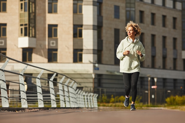 Jonge gezonde vrouw in sportkleding joggen langs de straat in de stad