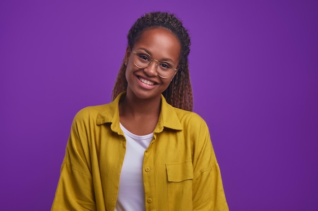 Jonge glimlachende aantrekkelijke afro-amerikaanse vrouw kijkt naar camerastands in de studio