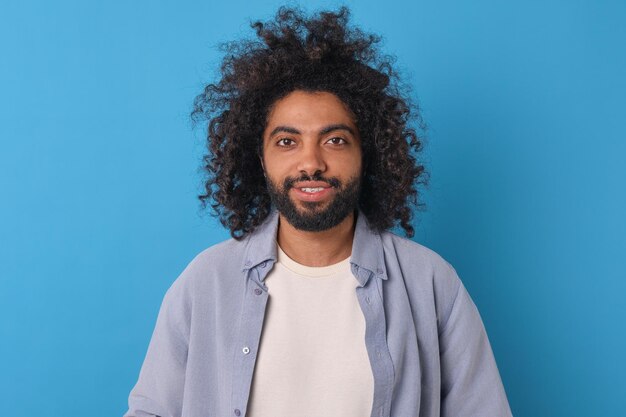 Jonge glimlachende Arabische man in casual shirt kijkt naar camera stands in de studio