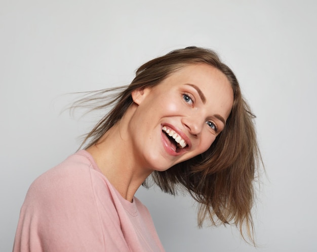 Jonge glimlachende blonde vrouw die een roze shirt draagt