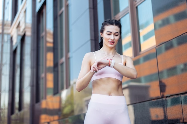 Jonge glimlachende fitte vrouw kijkt naar activiteit in een fitness armband na joggen in de stad