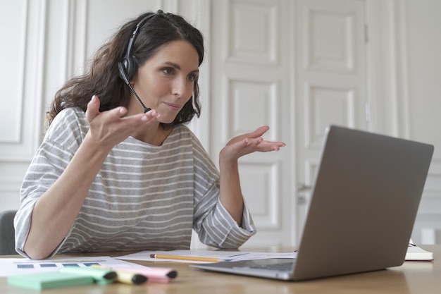 Jonge glimlachende Italiaanse vrouw freelancer in headset die klantklant raadpleegt via videogesprek