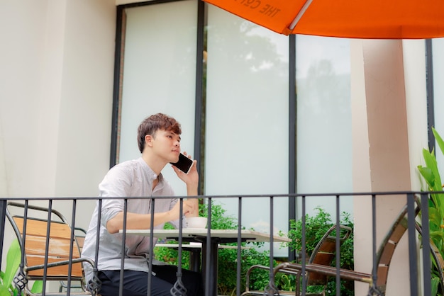 Jonge glimlachende man die aan de telefoon kijkt of een bericht leest in café buiten