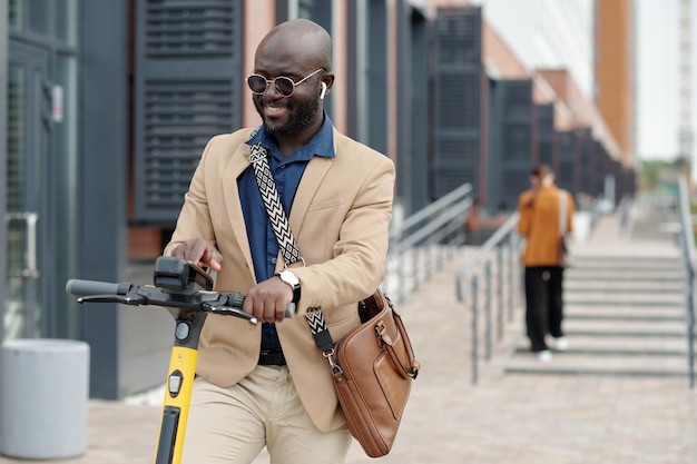 Jonge glimlachende mannelijke solopreneur in formele kleding die de instellingen van de scooter kiest