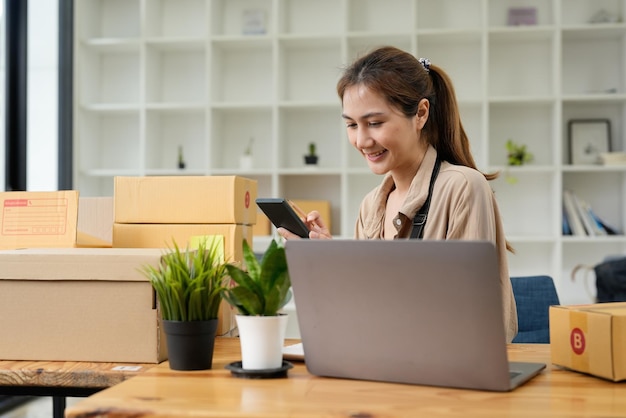 Jonge glimlachende mooie eigenaar aziatische vrouw freelance mkb-bedrijf online winkelen werken op laptopcomputer met pakketdoos op bureau thuis mkb-bedrijf online en leveringsconcept