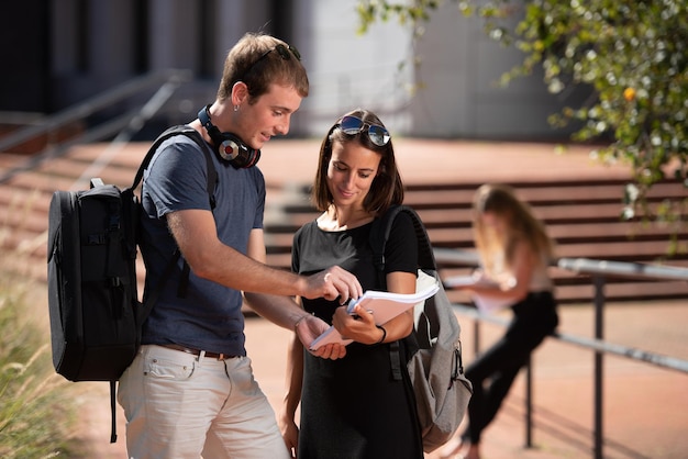 Jonge glimlachende studenten die rugzakken dragen die aan een notitieboekje buiten op de campus werken